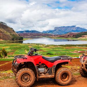 Turista en cuatrimoto roja frente a la laguna de Huaypo en el tour Maras Moray Cusco.