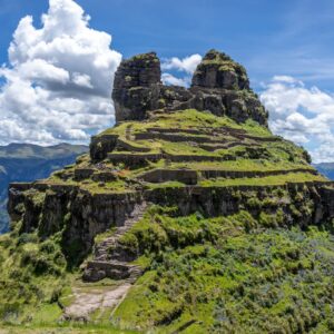 Vista aérea del sitio arqueológico de Waqrapukara, con formaciones de piedra en forma de cuerno y ruinas verdes en terrazas sobre una empinada montaña en Cusco.