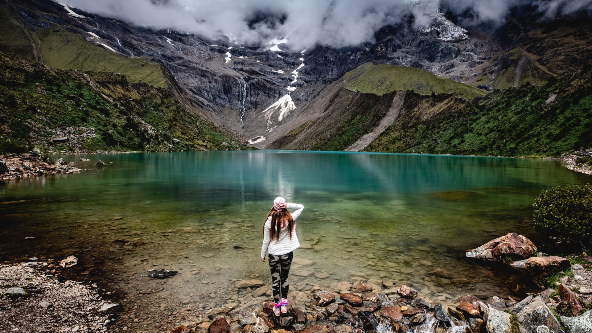 Uma turista contemplando as águas turquesas da Laguna Humantay sob o nevado Salkantay em Cusco, Peru.